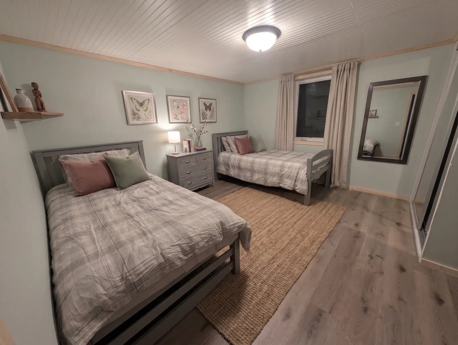 Furnished bedroom with two beds, a shared dresser, and a full-length mirror