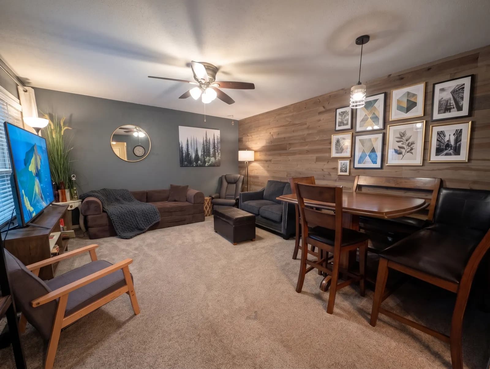 Living room with couches, a television, and a dining table beside a wood accent wall